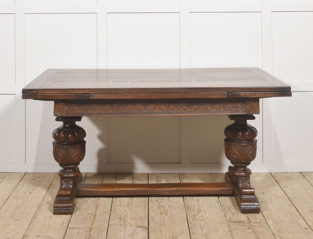 A dark carved oak refectory dining table featuring bulbous turned legs, a carved apron, and pull-out draw-leaf extensions. View II