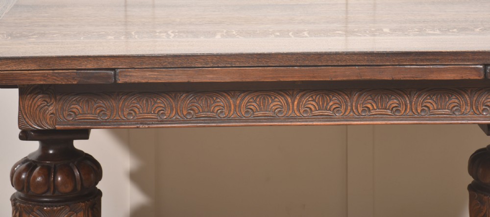 A dark carved oak refectory dining table featuring bulbous turned legs, a carved apron, and pull-out draw-leaf extensions. View III