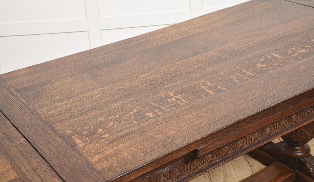 A dark carved oak refectory dining table featuring bulbous turned legs, a carved apron, and pull-out draw-leaf extensions. View IX