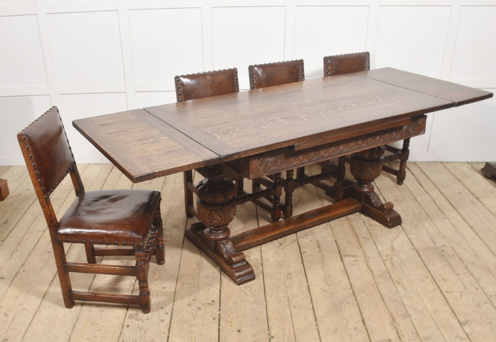 A dark carved oak refectory dining table featuring bulbous turned legs, a carved apron, and pull-out draw-leaf extensions. View X