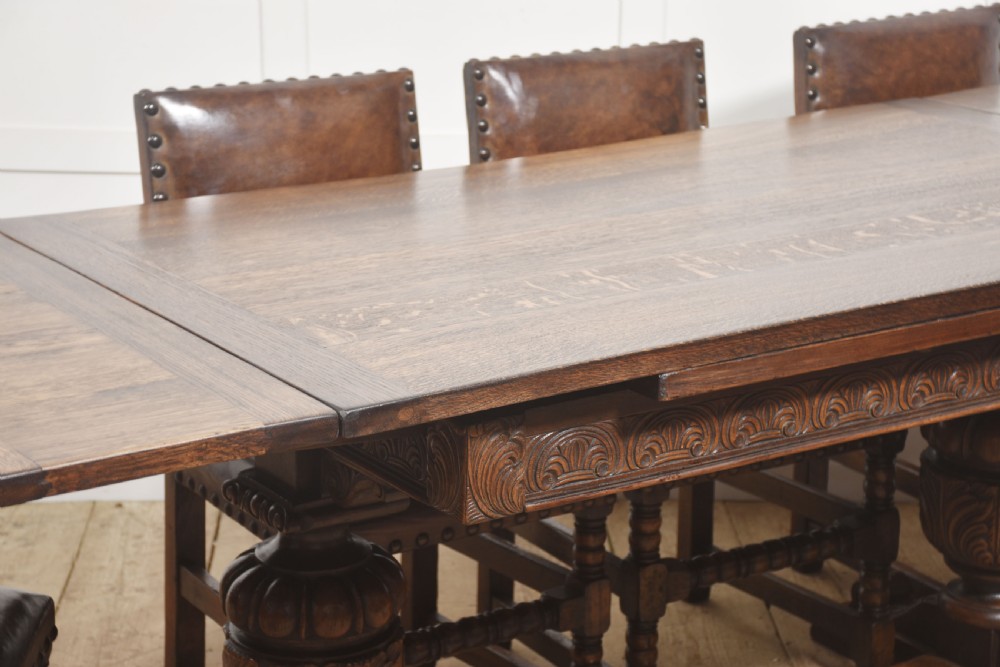 A dark carved oak refectory dining table featuring bulbous turned legs, a carved apron, and pull-out draw-leaf extensions. View XI