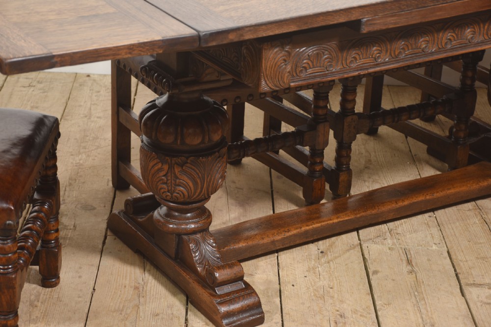 A dark carved oak refectory dining table featuring bulbous turned legs, a carved apron, and pull-out draw-leaf extensions. View XII