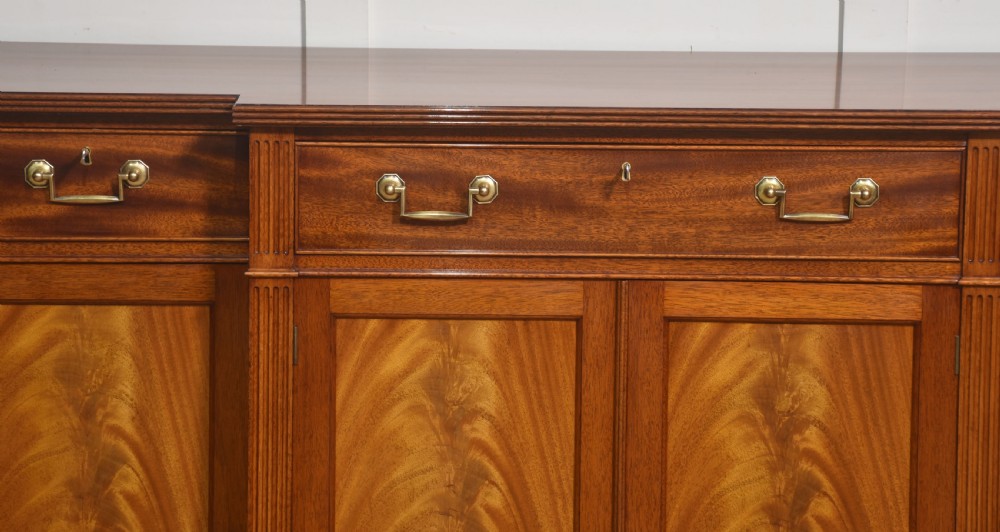 A flame mahogany breakfront sideboard featuring four panelled cupboard doors, four top drawers with brass drop handles, and fluted pilasters. View II