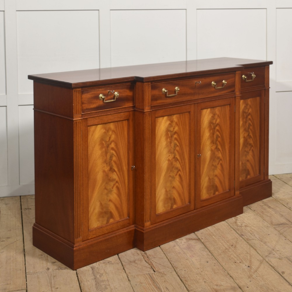 A flame mahogany breakfront sideboard featuring four panelled cupboard doors, four top drawers with brass drop handles, and fluted pilasters. View III