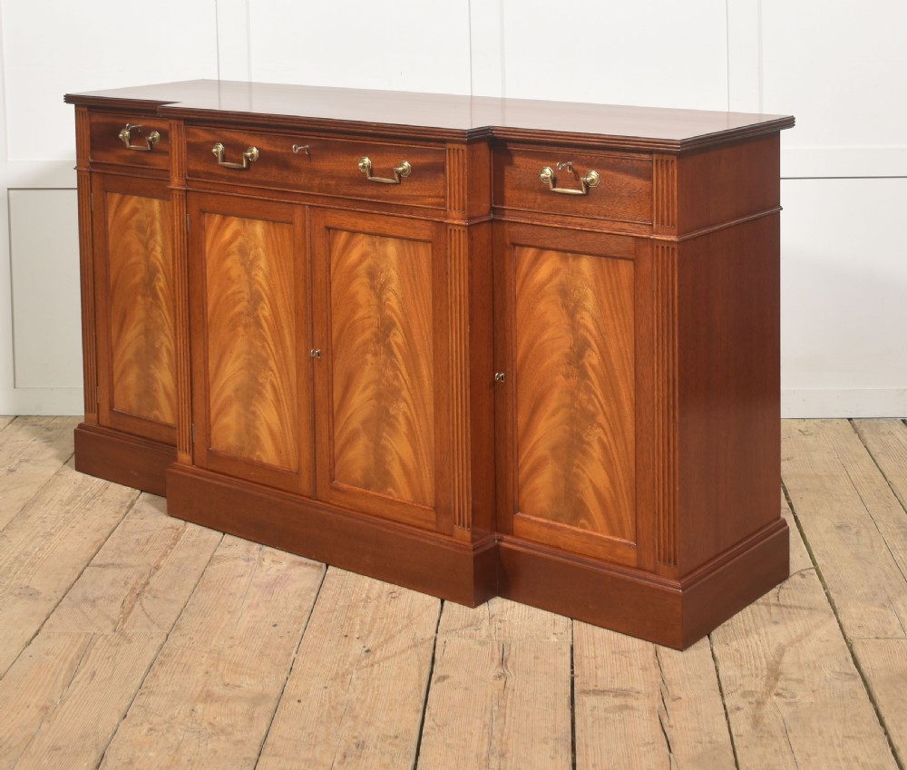 A flame mahogany breakfront sideboard featuring four panelled cupboard doors, four top drawers with brass drop handles, and fluted pilasters. View V