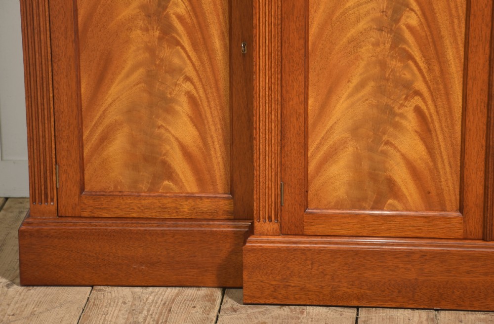 A flame mahogany breakfront sideboard featuring four panelled cupboard doors, four top drawers with brass drop handles, and fluted pilasters. View VI