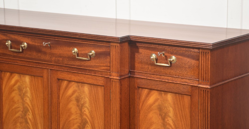 A flame mahogany breakfront sideboard featuring four panelled cupboard doors, four top drawers with brass drop handles, and fluted pilasters. View VII