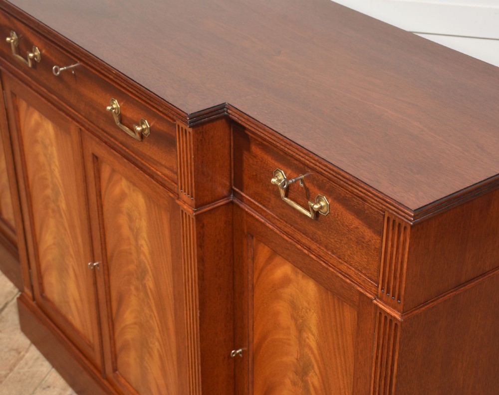 A flame mahogany breakfront sideboard featuring four panelled cupboard doors, four top drawers with brass drop handles, and fluted pilasters. View VIII