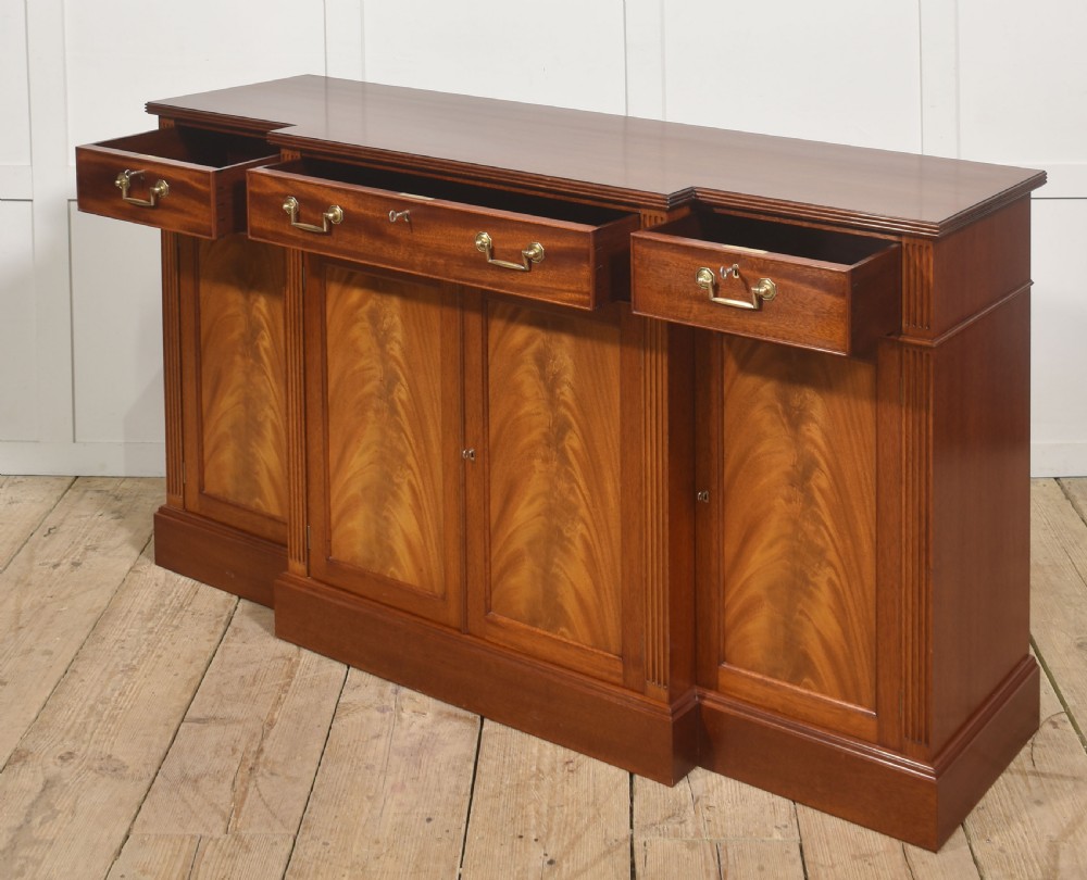 A flame mahogany breakfront sideboard featuring four panelled cupboard doors, four top drawers with brass drop handles, and fluted pilasters. View IX