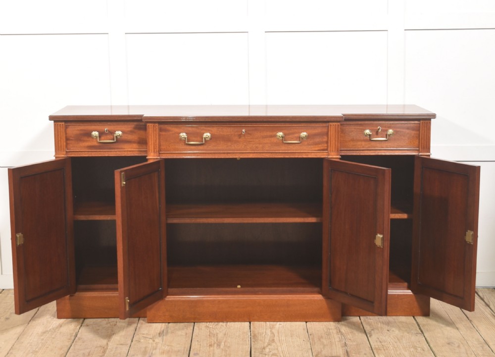 A flame mahogany breakfront sideboard featuring four panelled cupboard doors, four top drawers with brass drop handles, and fluted pilasters. View X