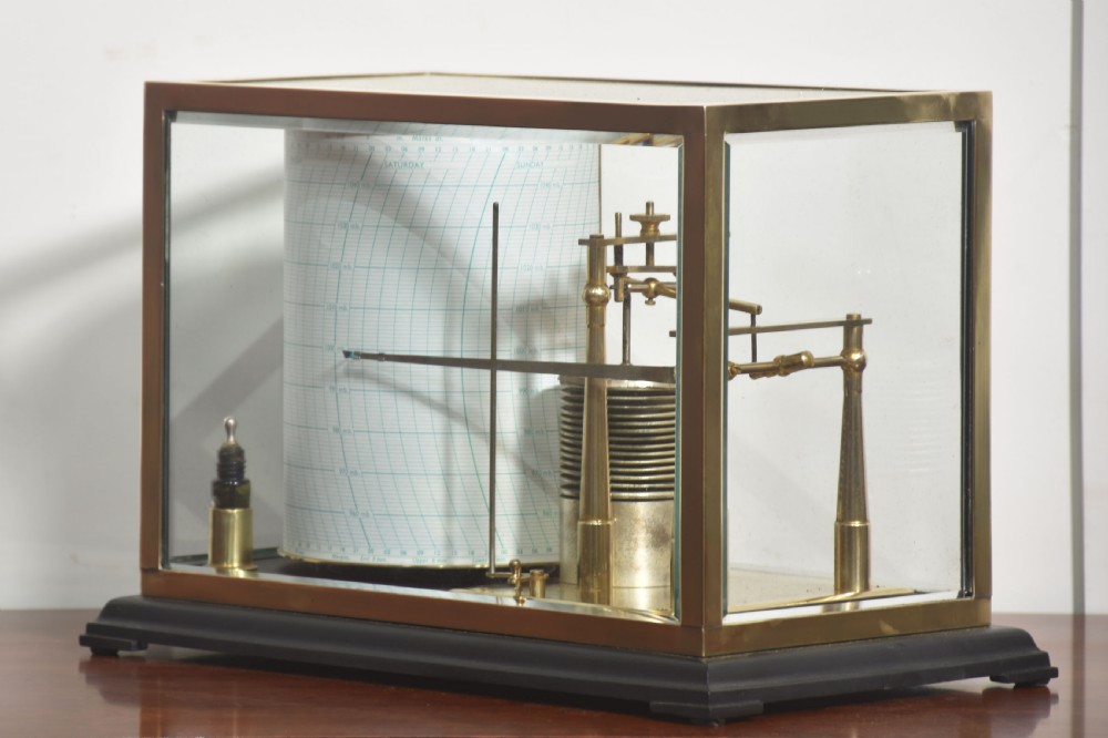 An antique brass-framed glass display case housing a scientific barograph mechanism with a paper chart drum, aneroid capsules, and pen arm. View III