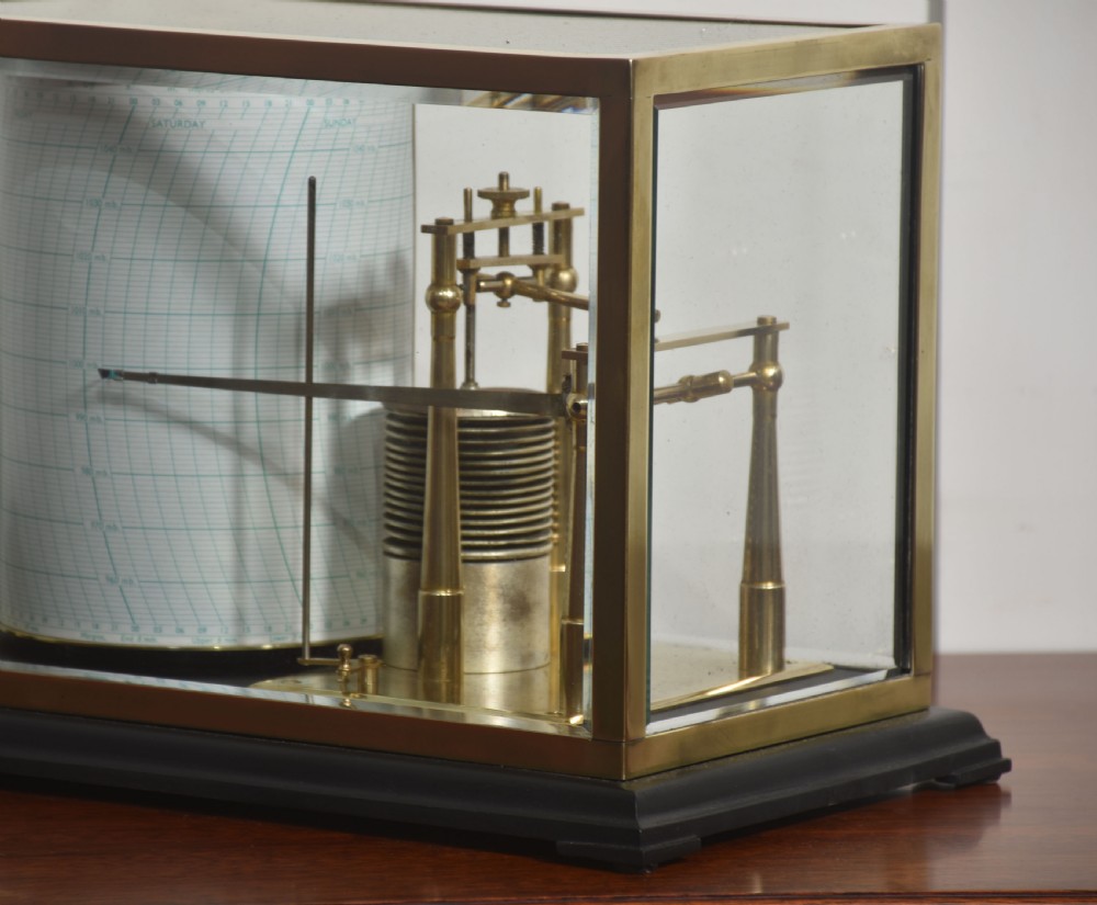 An antique brass-framed glass display case housing a scientific barograph mechanism with a paper chart drum, aneroid capsules, and pen arm. View IV
