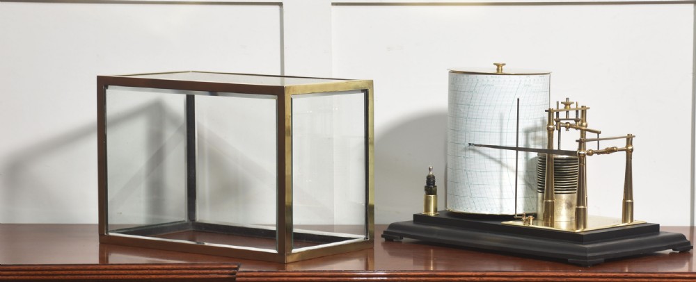 An antique brass-framed glass display case housing a scientific barograph mechanism with a paper chart drum, aneroid capsules, and pen arm. View V