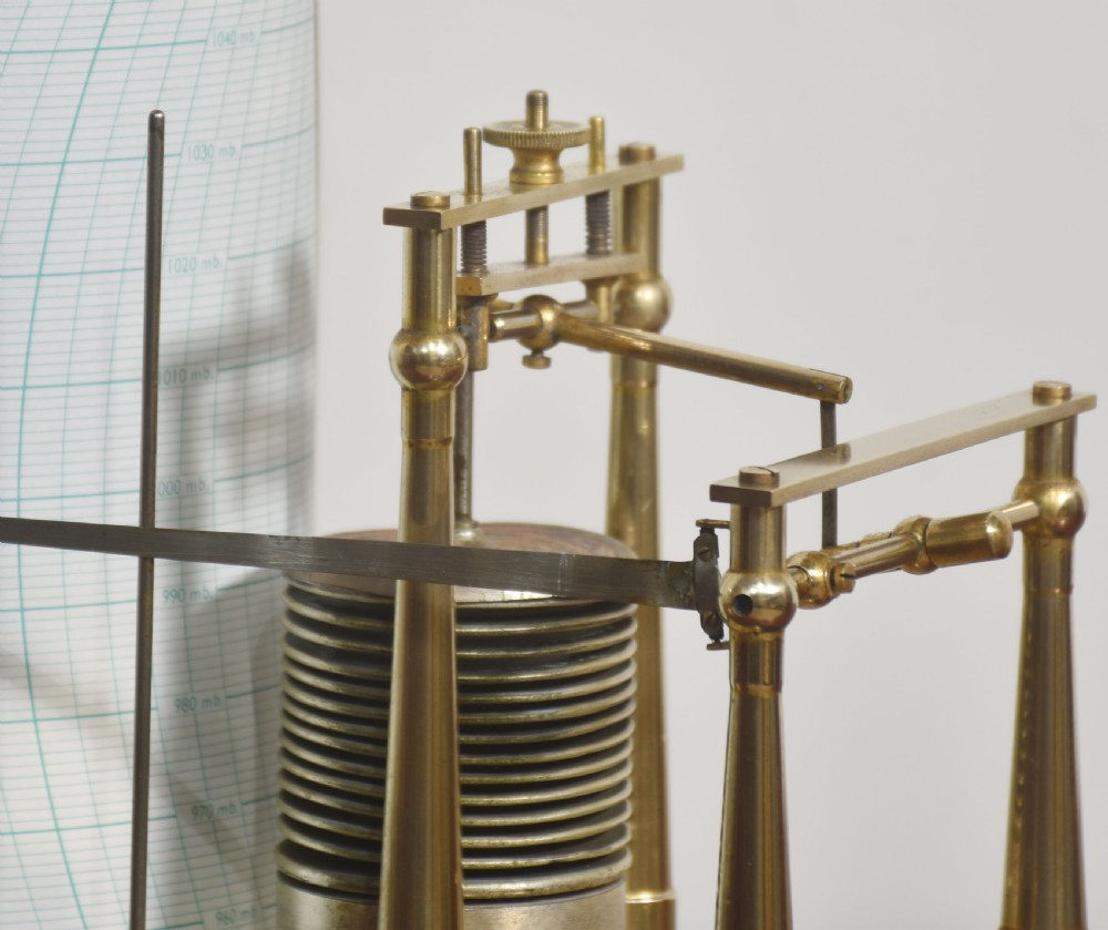 An antique brass-framed glass display case housing a scientific barograph mechanism with a paper chart drum, aneroid capsules, and pen arm. View VII