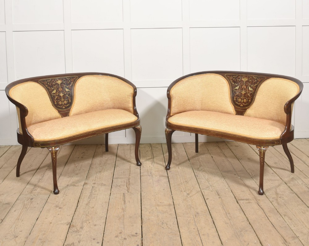A matching pair of Edwardian mahogany settees featuring curved backs, floral marquetry central splats, and pale mustard yellow upholstered seats.