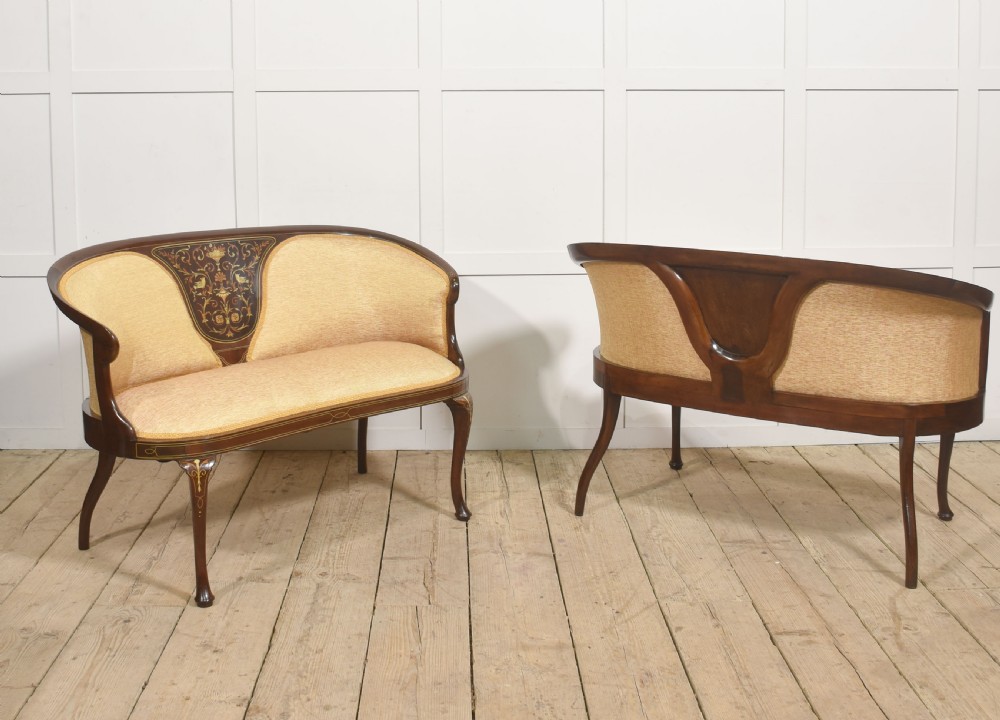 A matching pair of Edwardian mahogany settees featuring curved backs, floral marquetry central splats, and pale mustard yellow upholstered seats. View III