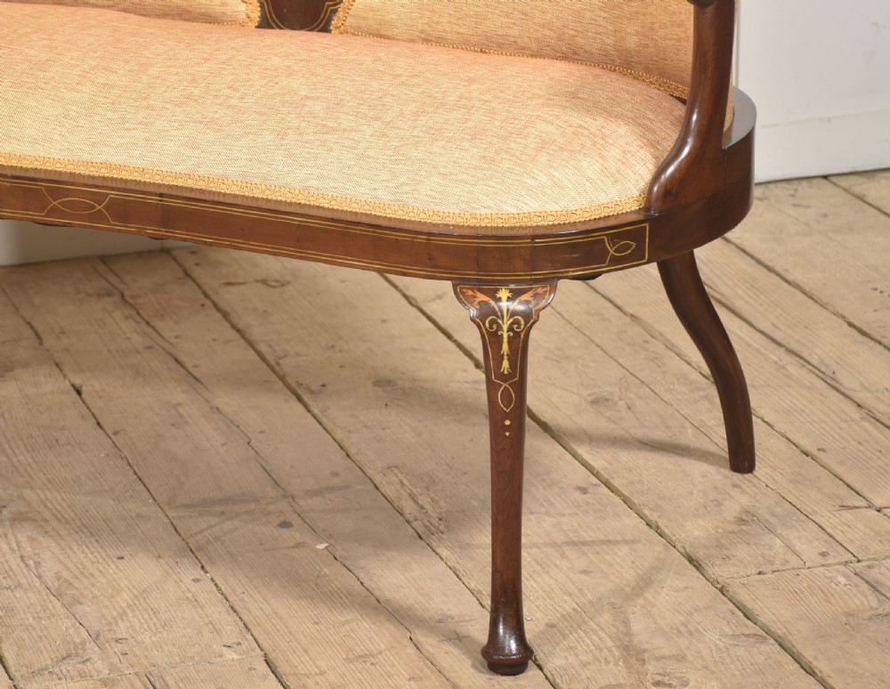 A matching pair of Edwardian mahogany settees featuring curved backs, floral marquetry central splats, and pale mustard yellow upholstered seats. View IV