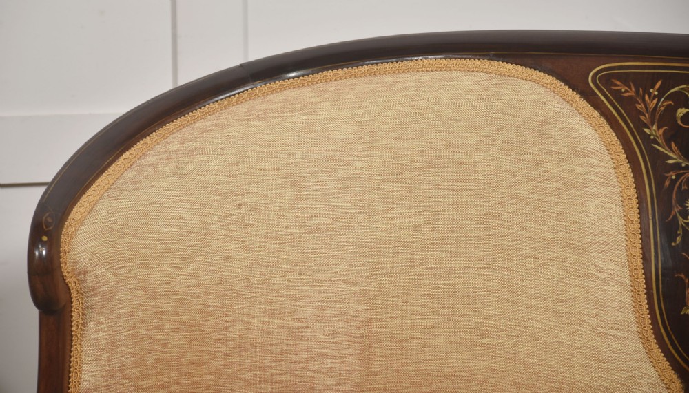 A matching pair of Edwardian mahogany settees featuring curved backs, floral marquetry central splats, and pale mustard yellow upholstered seats. View V