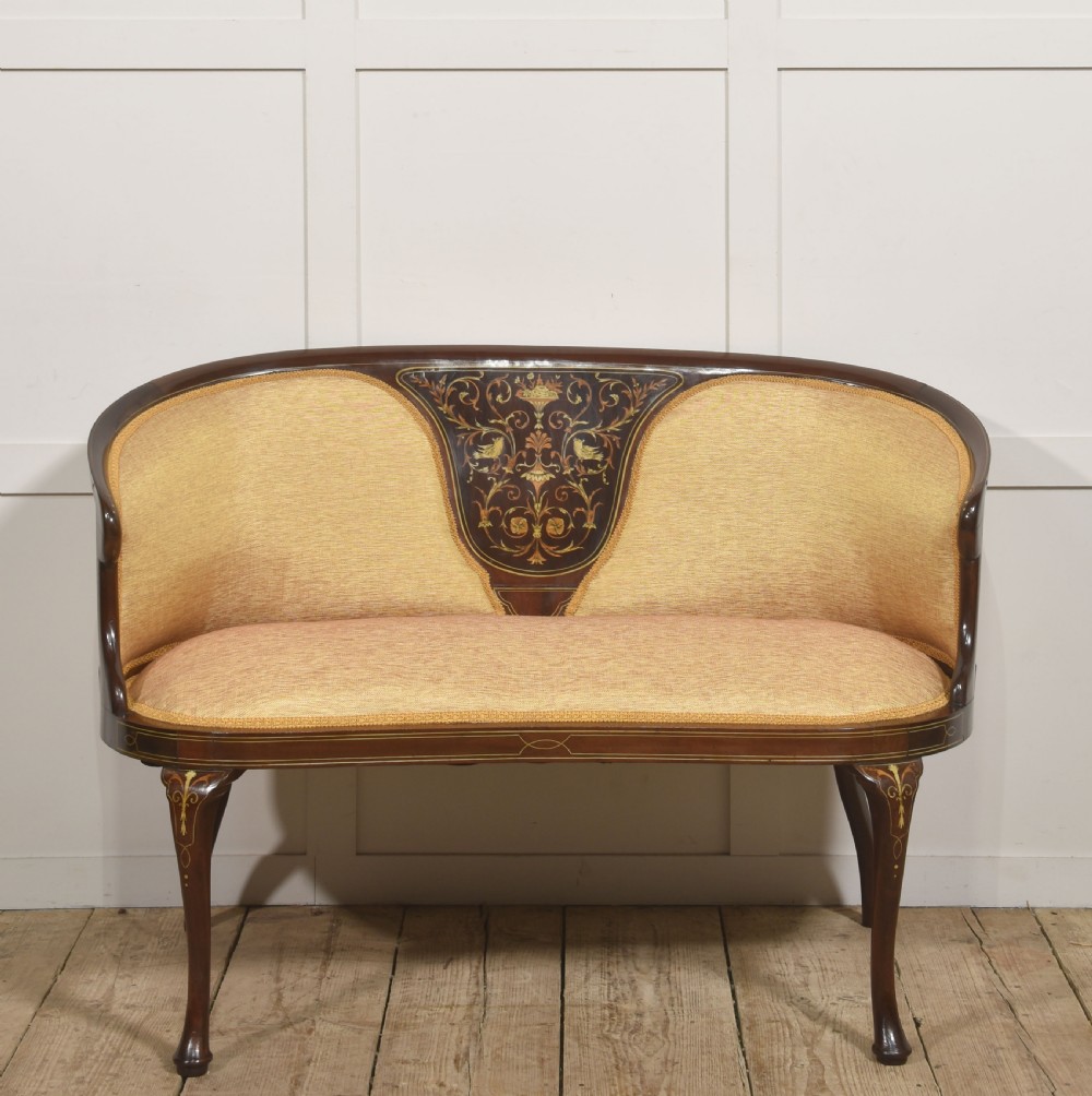 A matching pair of Edwardian mahogany settees featuring curved backs, floral marquetry central splats, and pale mustard yellow upholstered seats. View VIII