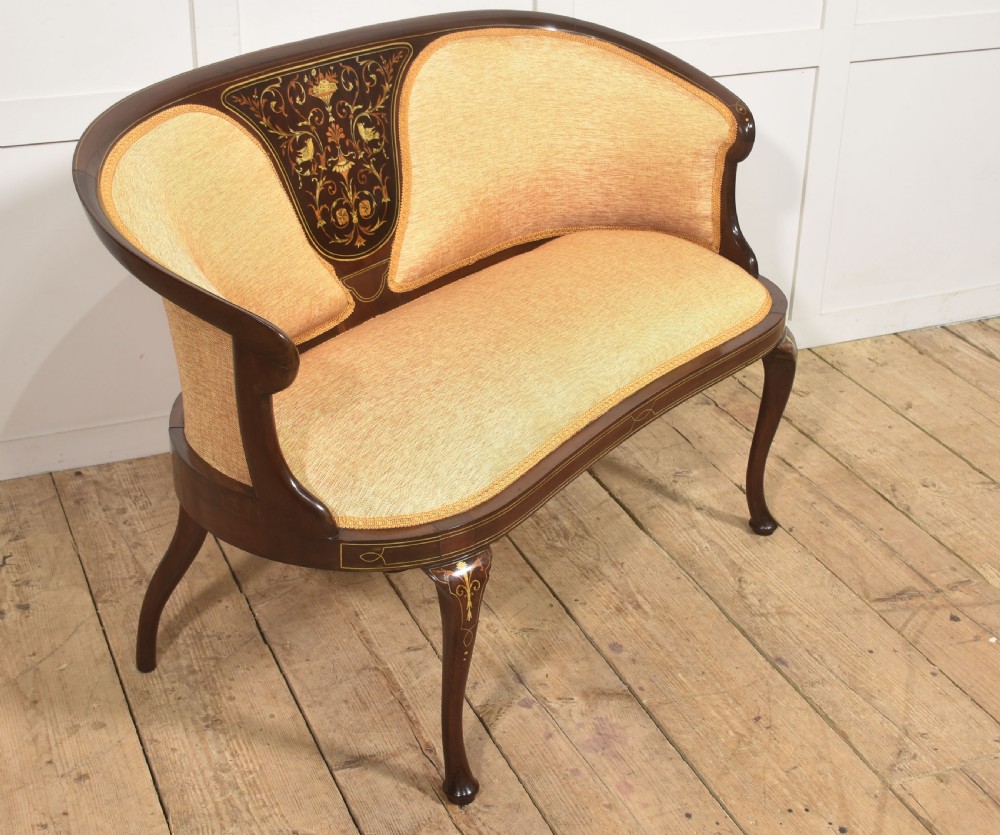 A matching pair of Edwardian mahogany settees featuring curved backs, floral marquetry central splats, and pale mustard yellow upholstered seats. View IX