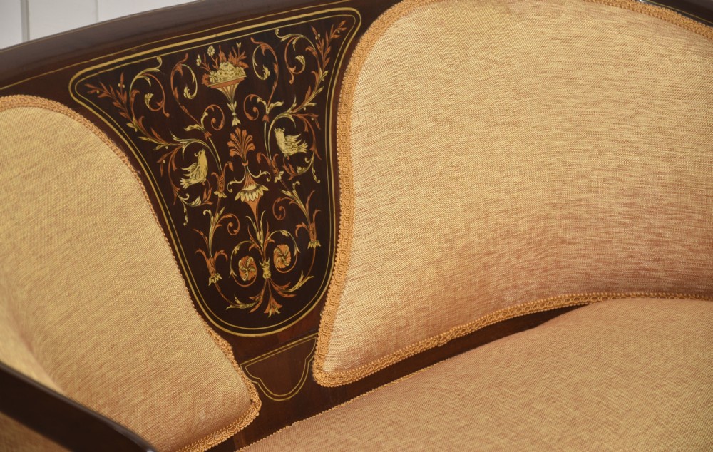 A matching pair of Edwardian mahogany settees featuring curved backs, floral marquetry central splats, and pale mustard yellow upholstered seats. View X