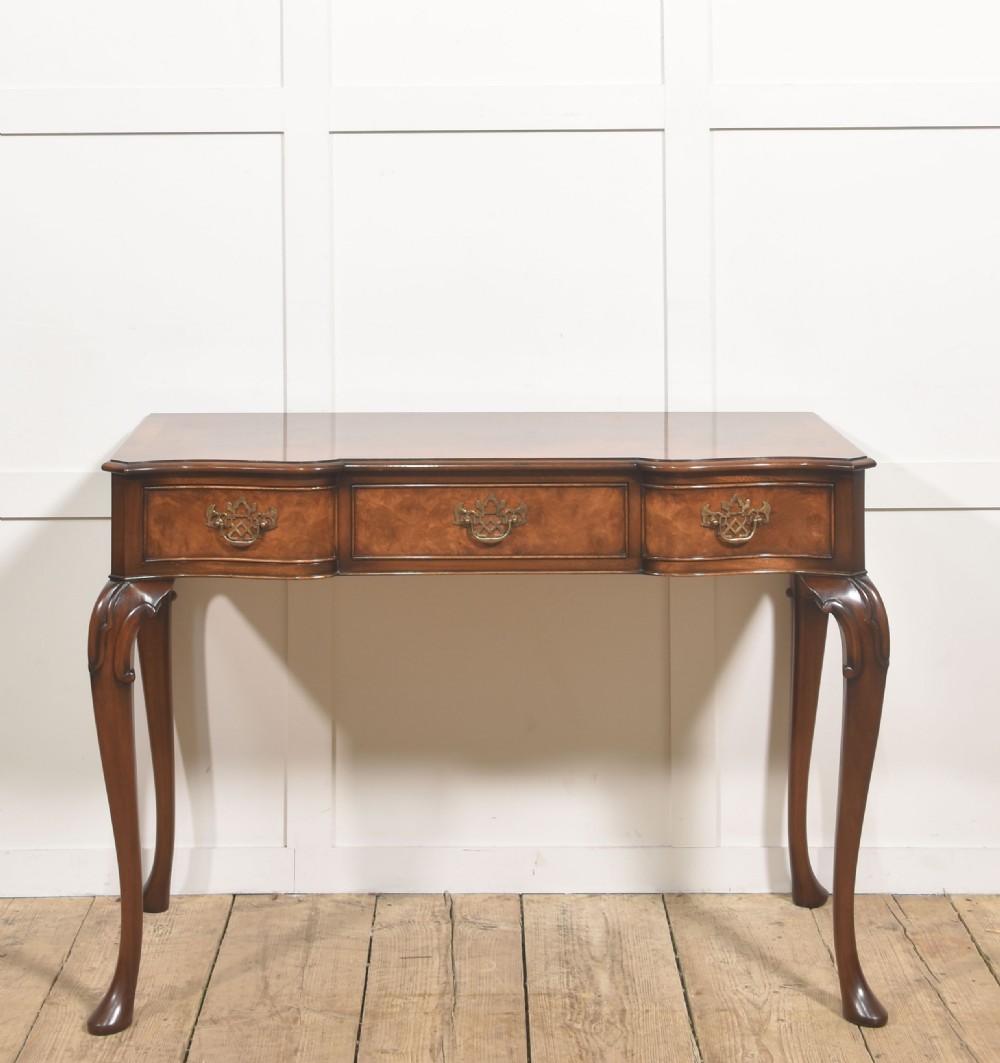 A burr walnut writing table featuring three drawers with brass handles and slender cabriole legs.