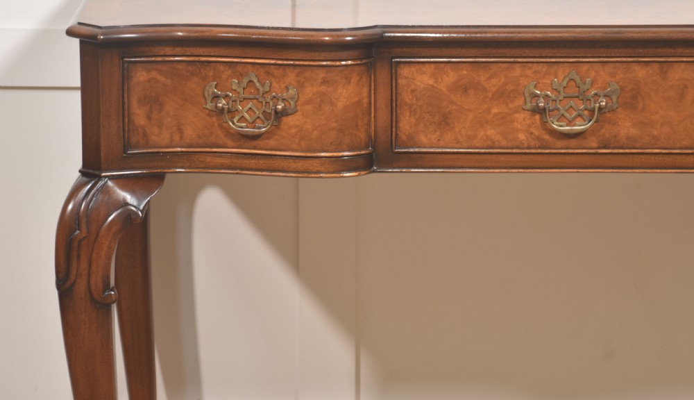 A burr walnut writing table featuring three drawers with brass handles and slender cabriole legs. View IV