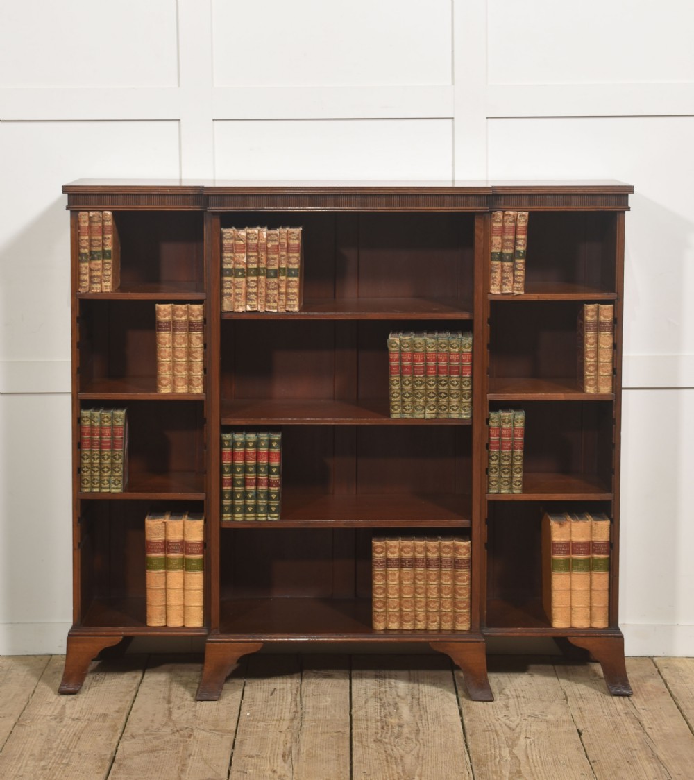 A low mahogany breakfront open bookcase featuring a reeded frieze top, adjustable shelf sections, and bracket feet.