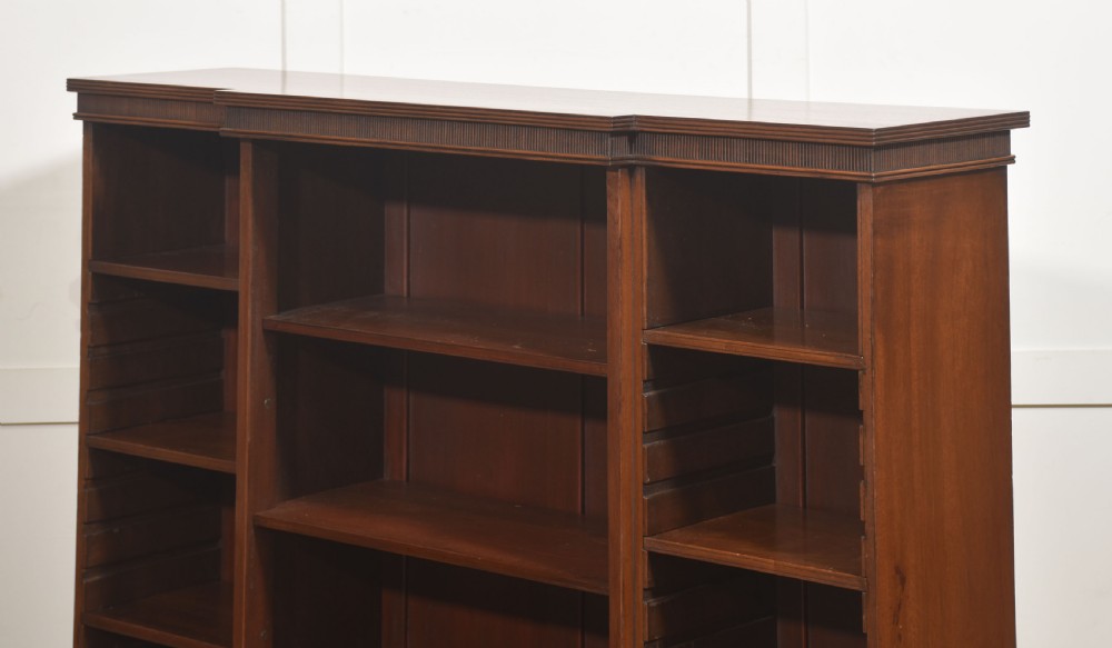 A low mahogany breakfront open bookcase featuring a reeded frieze top, adjustable shelf sections, and bracket feet. View X