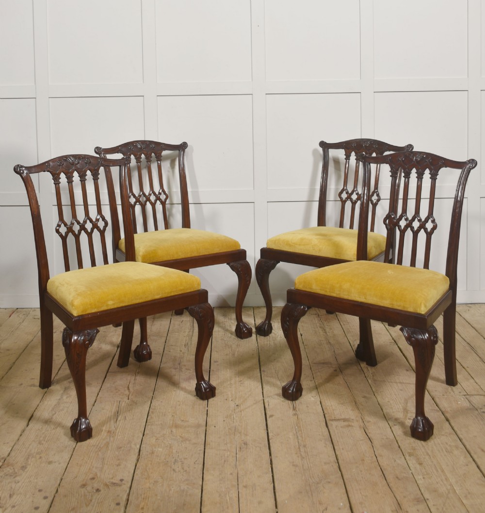 Set of four dark mahogany dining chairs featuring carved pierced splats, yellow velvet upholstered seats, and cabriole front legs with ball and claw feet.