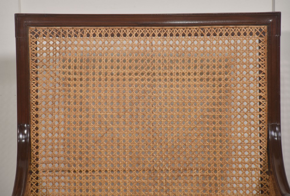 A mahogany bergere armchair with woven rattan cane side panels, turned front arm supports, and button-tufted sage green velvet cushions. View VII