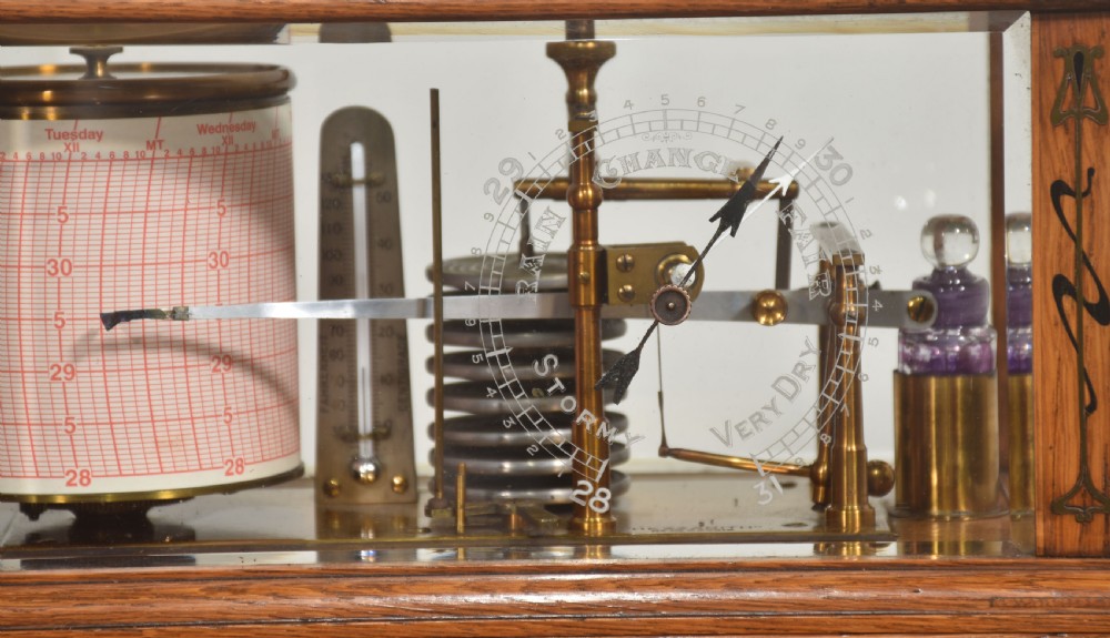 An Edwardian oak-cased barograph featuring bevelled glass panels, polished brass movement, paper chart drum, and floral Art Nouveau wood inlay along the base drawer and corner pillars. View II