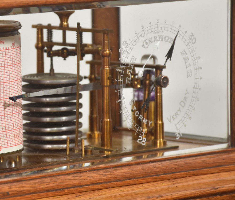 An Edwardian oak-cased barograph featuring bevelled glass panels, polished brass movement, paper chart drum, and floral Art Nouveau wood inlay along the base drawer and corner pillars. View IV
