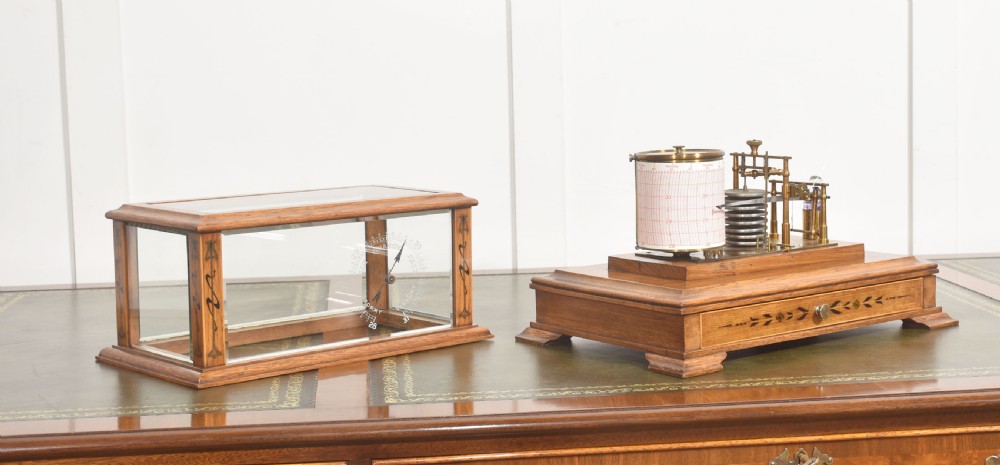 An Edwardian oak-cased barograph featuring bevelled glass panels, polished brass movement, paper chart drum, and floral Art Nouveau wood inlay along the base drawer and corner pillars. View V