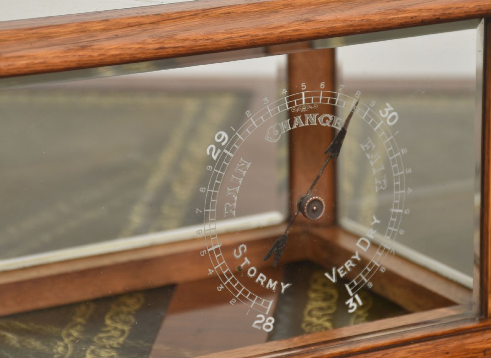 An Edwardian oak-cased barograph featuring bevelled glass panels, polished brass movement, paper chart drum, and floral Art Nouveau wood inlay along the base drawer and corner pillars. View VIII