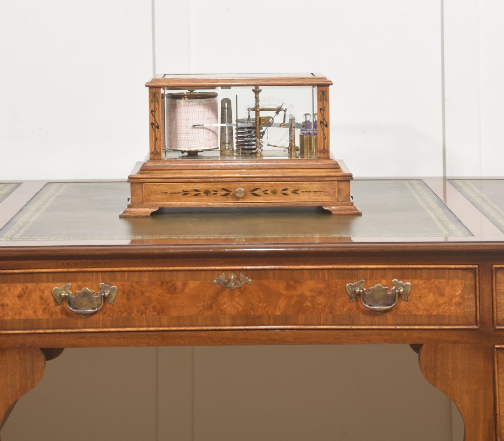 An Edwardian oak-cased barograph featuring bevelled glass panels, polished brass movement, paper chart drum, and floral Art Nouveau wood inlay along the base drawer and corner pillars. View X