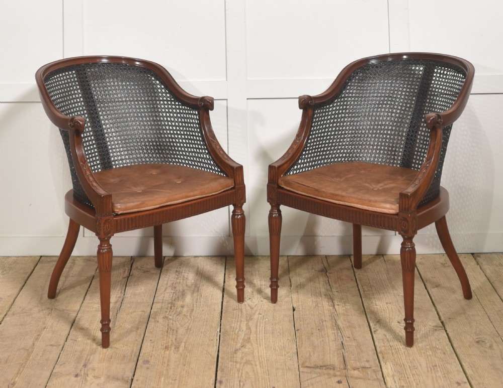 A pair of Regency style dark mahogany bergere armchairs featuring woven cane backs and tan leather buttoned seat cushions.