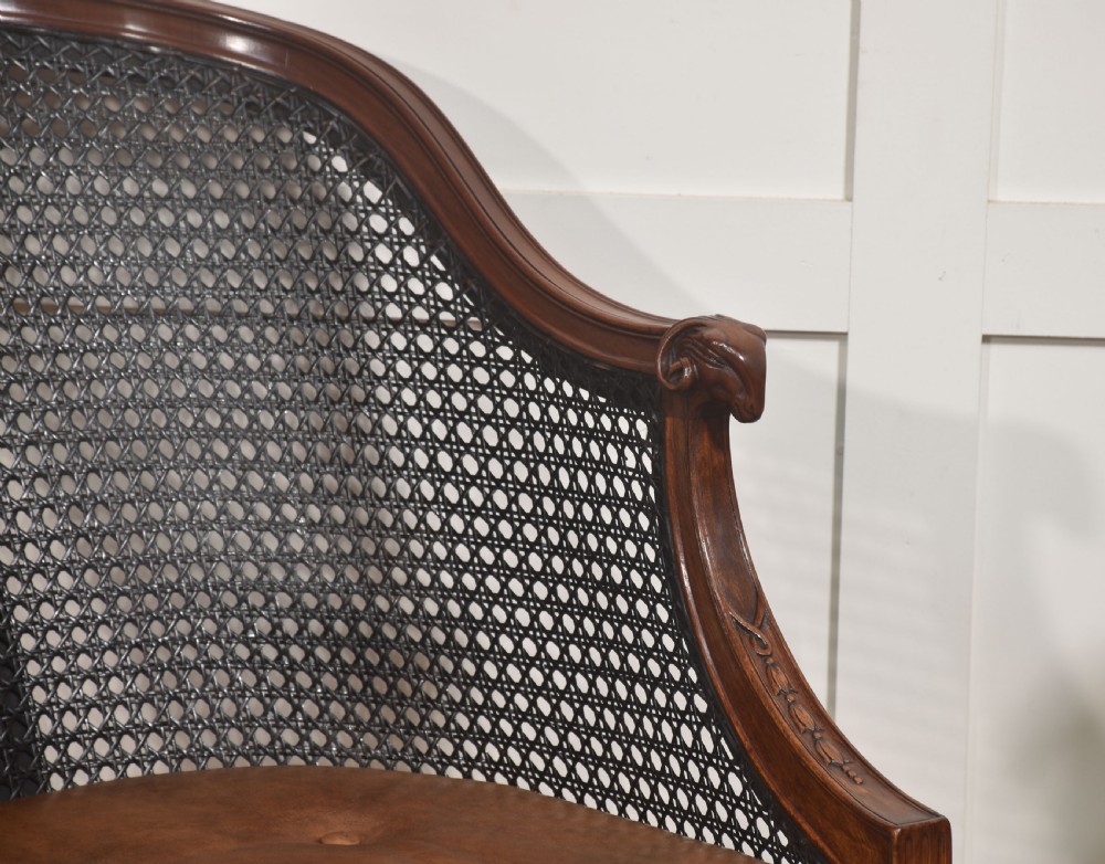 A pair of Regency style dark mahogany bergere armchairs featuring woven cane backs and tan leather buttoned seat cushions. View IV