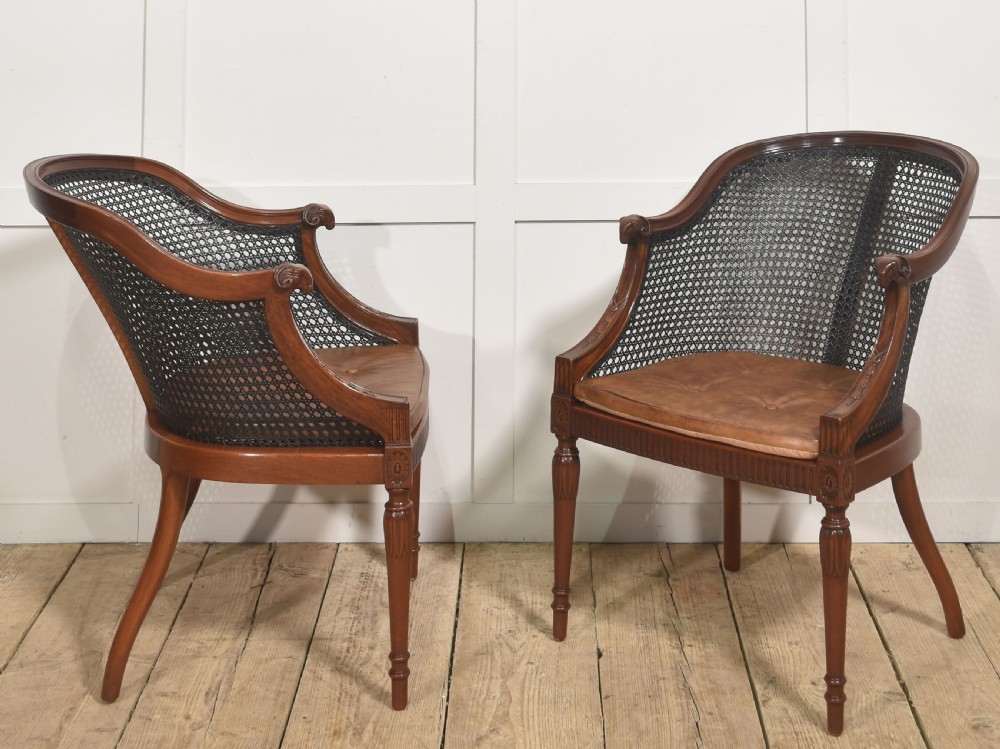 A pair of Regency style dark mahogany bergere armchairs featuring woven cane backs and tan leather buttoned seat cushions. View V