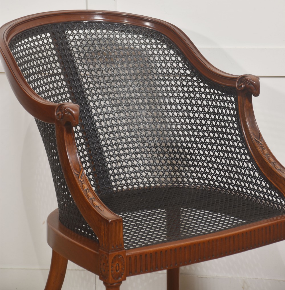 A pair of Regency style dark mahogany bergere armchairs featuring woven cane backs and tan leather buttoned seat cushions. View VII