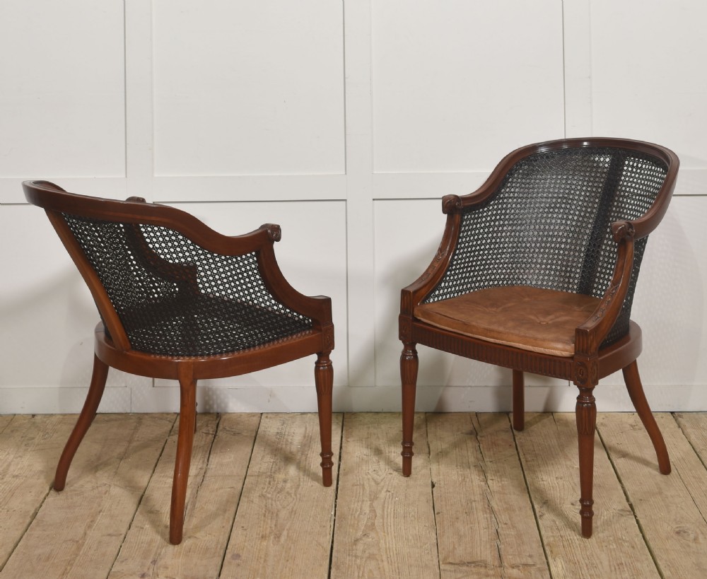 A pair of Regency style dark mahogany bergere armchairs featuring woven cane backs and tan leather buttoned seat cushions. View VIII