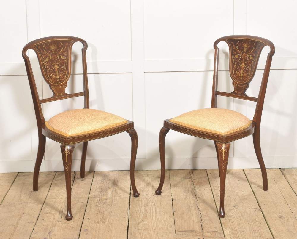 A pair of Edwardian inlaid mahogany side chairs with vase-shaped marquetry splats, cabriole front legs, and golden upholstered seats.