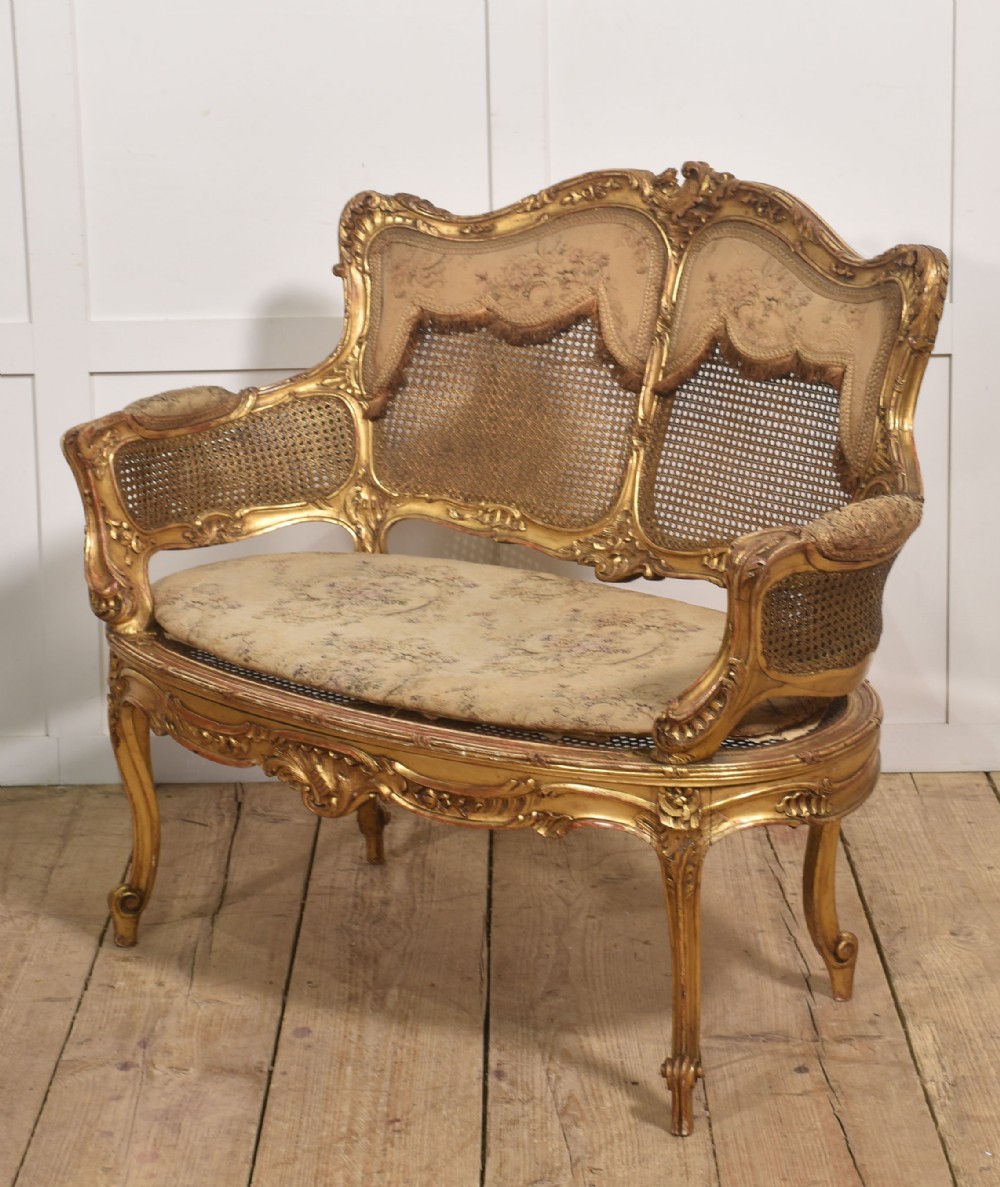 A French Louis XV style giltwood canape featuring a carved frame, caned back and sides, cabriole legs, and an upholstered seat cushion.
