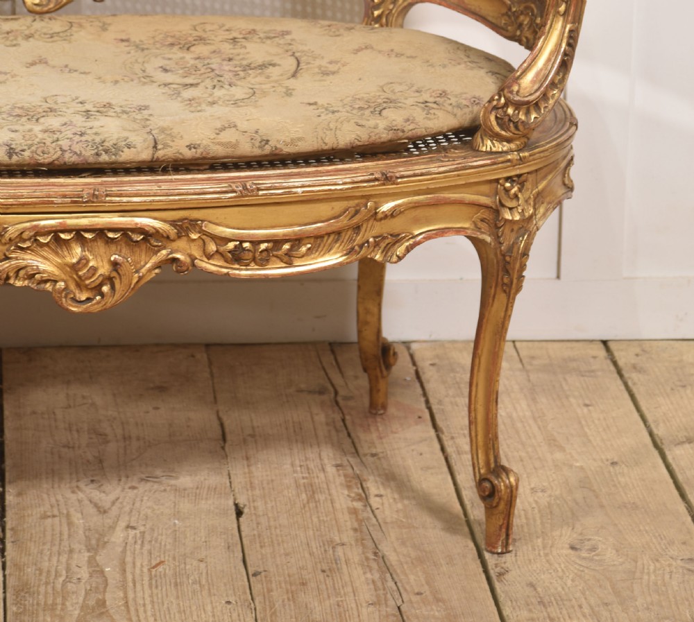 A French Louis XV style giltwood canape featuring a carved frame, caned back and sides, cabriole legs, and an upholstered seat cushion. View IV