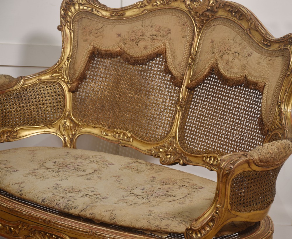 A French Louis XV style giltwood canape featuring a carved frame, caned back and sides, cabriole legs, and an upholstered seat cushion. View V