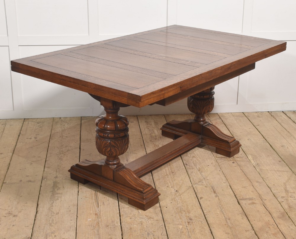 A solid oak refectory dining table featuring a rectangular planked top supported by two carved cup-and-cover pedestal legs connected by a central stretcher. View II