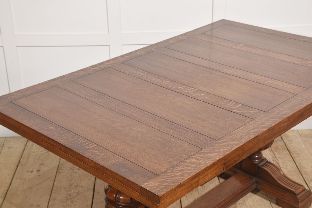 A solid oak refectory dining table featuring a rectangular planked top supported by two carved cup-and-cover pedestal legs connected by a central stretcher. View V