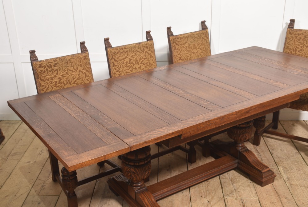 A solid oak refectory dining table featuring a rectangular planked top supported by two carved cup-and-cover pedestal legs connected by a central stretcher. View VII