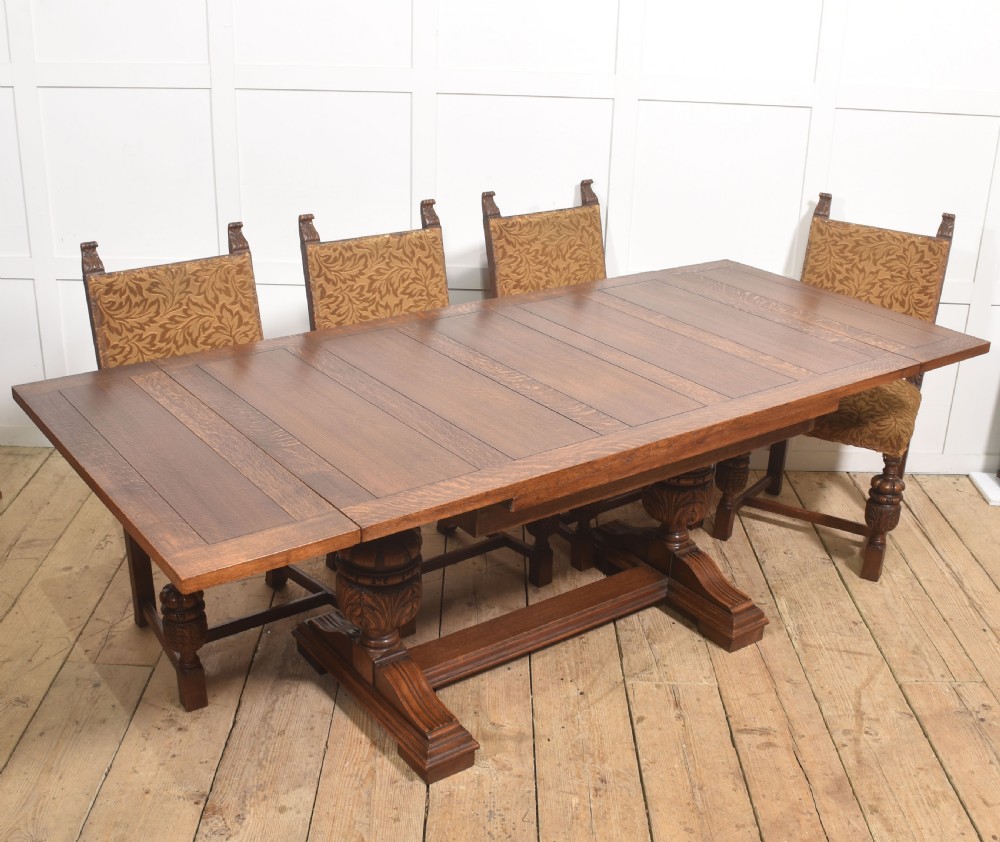 A solid oak refectory dining table featuring a rectangular planked top supported by two carved cup-and-cover pedestal legs connected by a central stretcher. View VIII