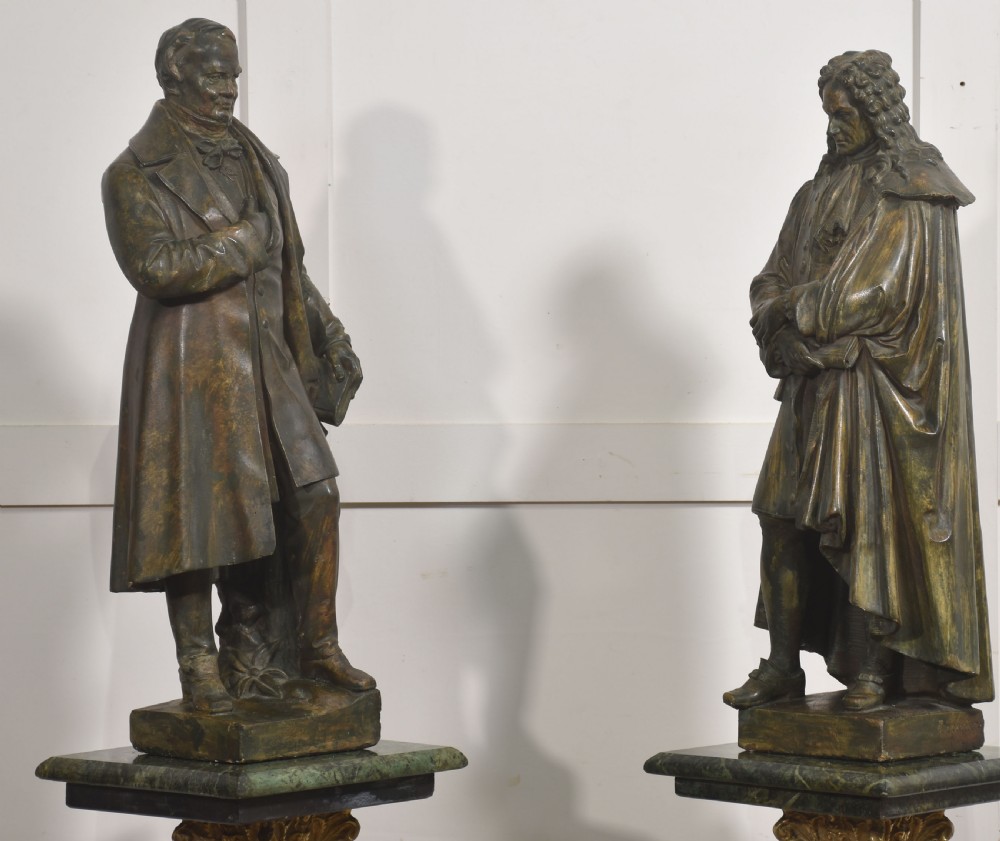 A pair of late nineteenth-century patinated chalkware statues depicting two standing male figures in historical attire on integral rectangular bases.